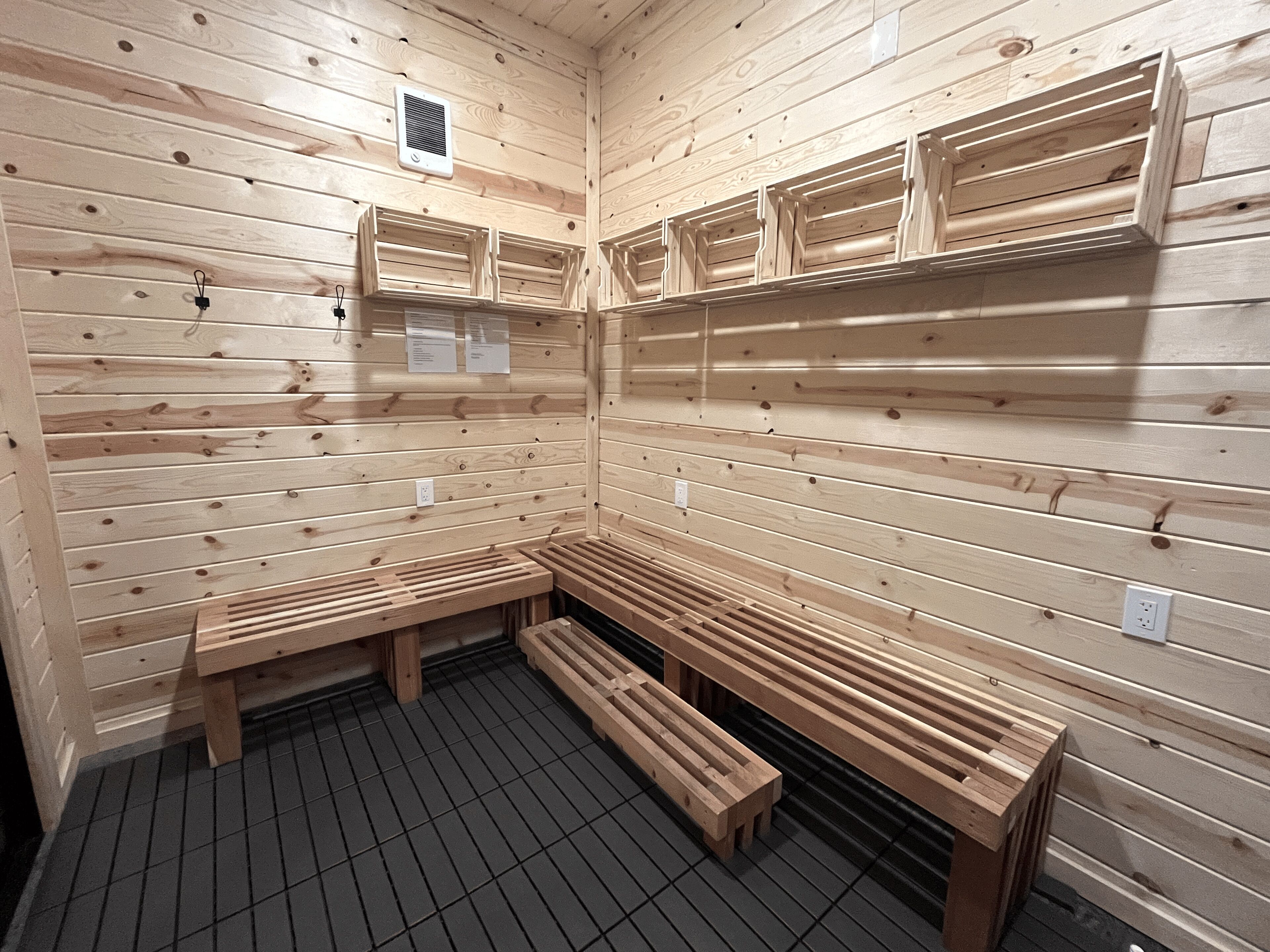 A sauna with wooden benches and benches, a tiled floor, and a vent on the ceiling.