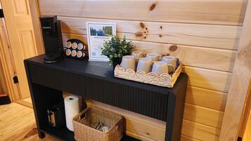 Ein schwarzer Konsolentisch mit einer Keurig-Kaffeemaschine, einem gerahmten Willkommensschild, einer kleinen Topfpflanze und einem Korb mit Tassen.