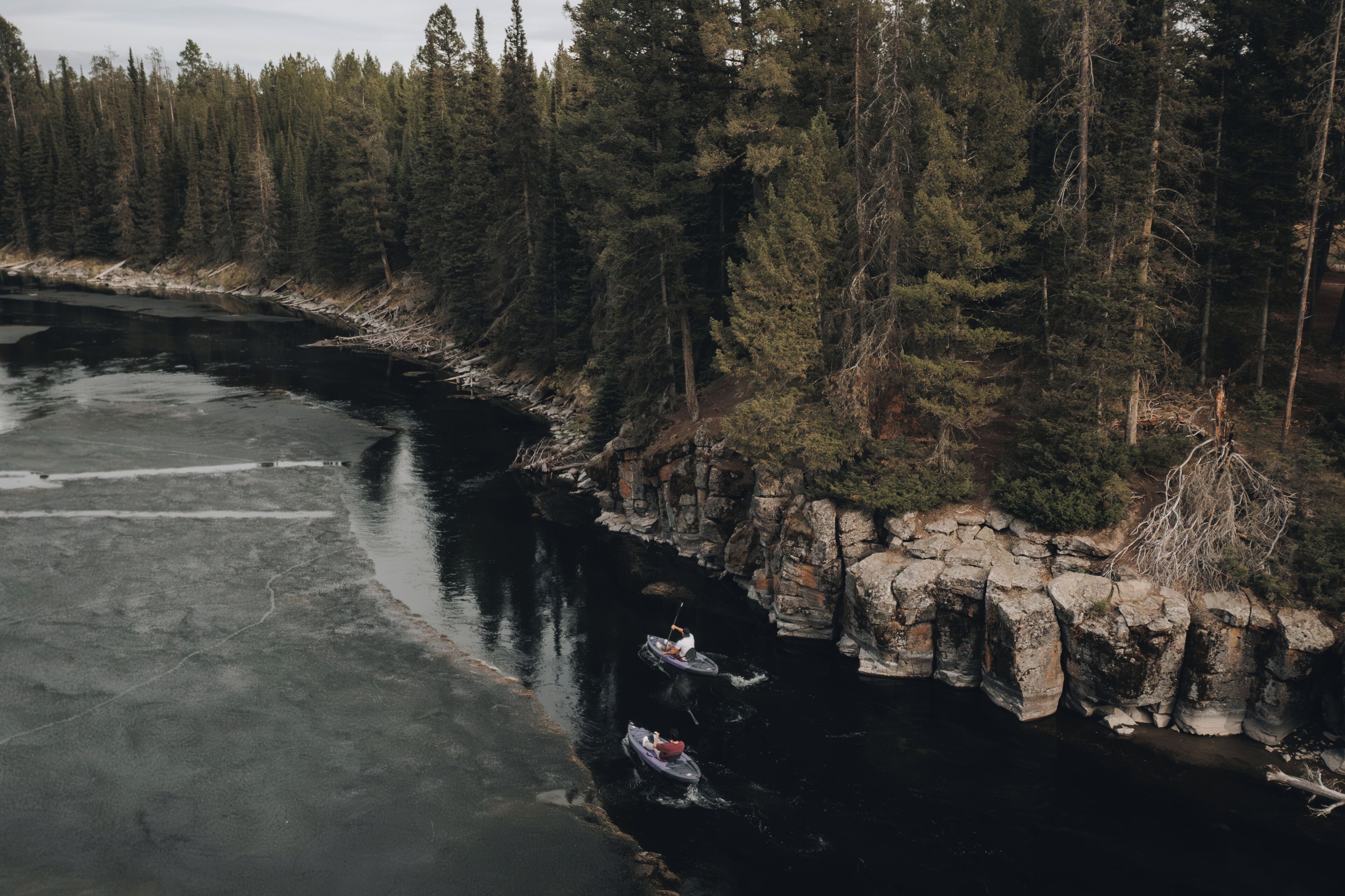 A river with two canoes, surrounded by dense forest and rocky cliffs.