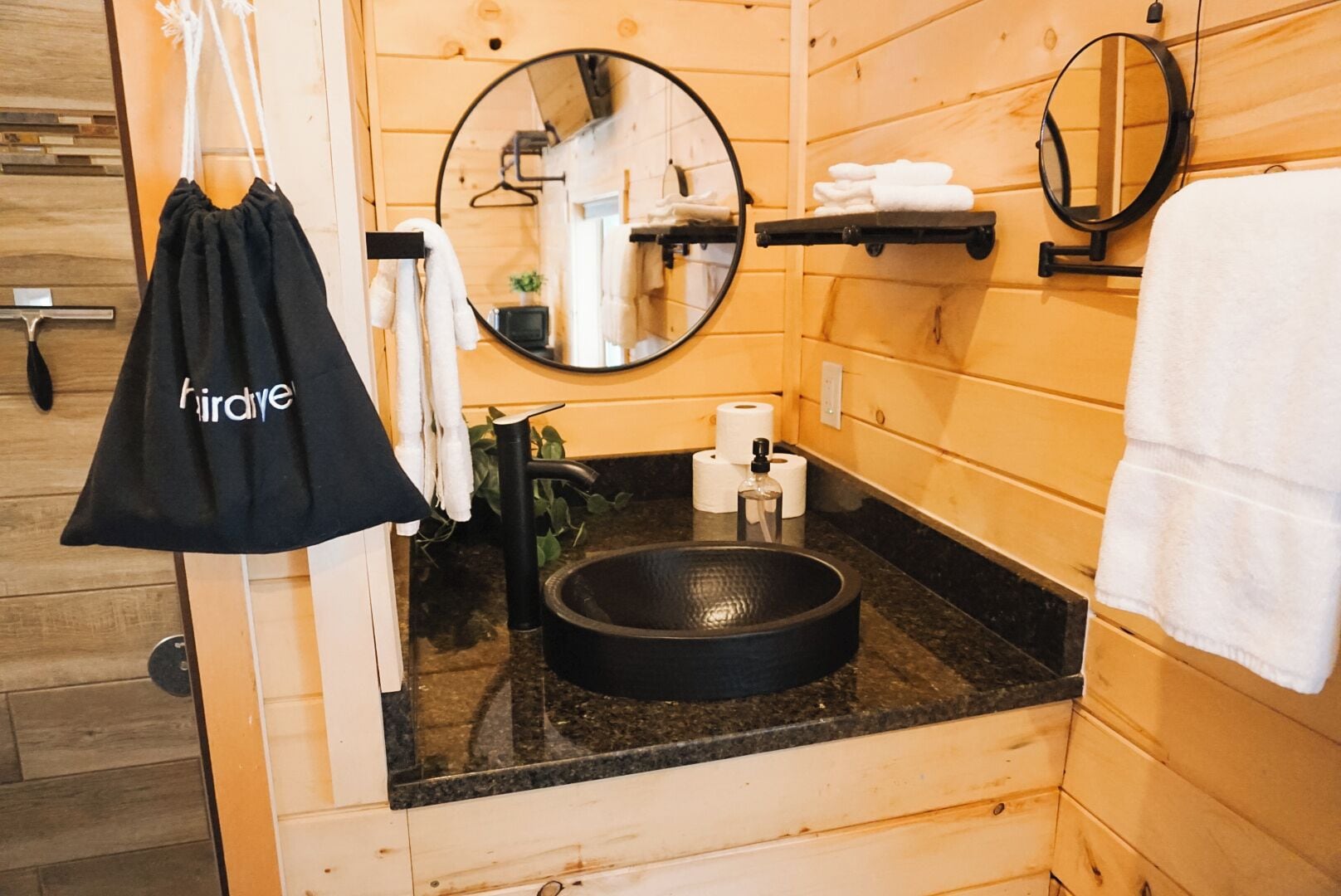 Een badkamer in chaletstijl met houten details, een rond wastafeltje, twee spiegels en een handdoekrek.