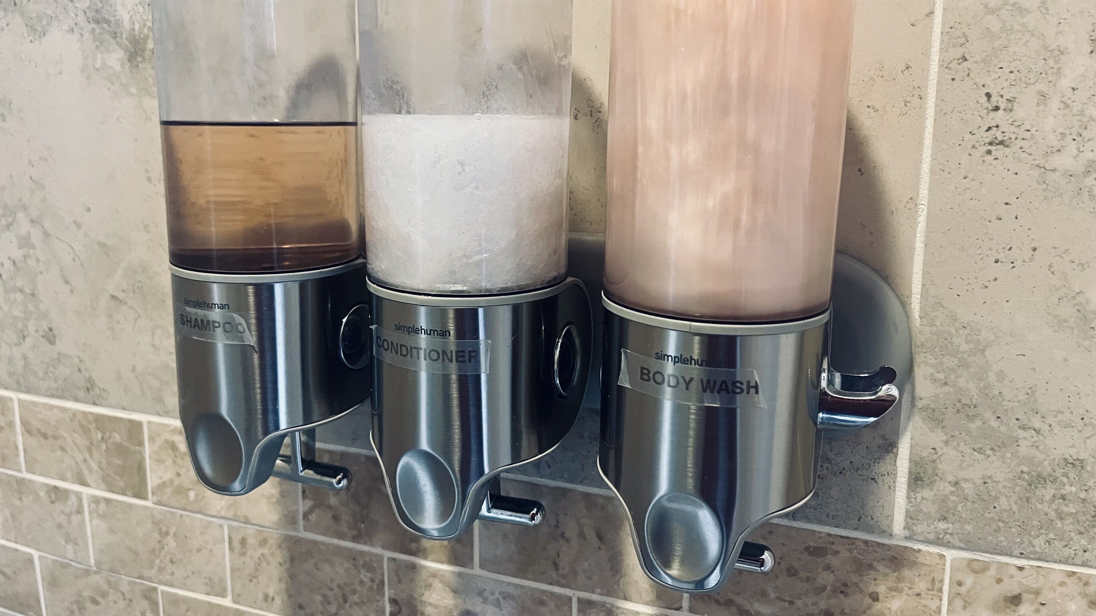 A wall-mounted dispenser with three different liquid options labeled as 'SHAMPOO', 'CONDITIONER', and 'BODY WASH'.
