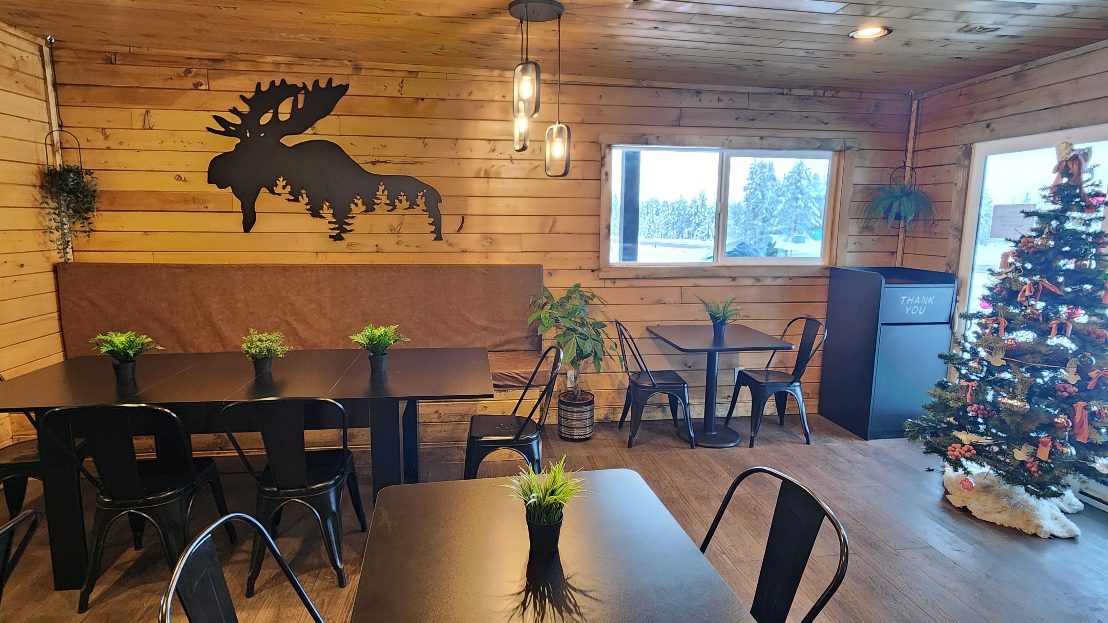 Un restaurante acogedor de estilo cabaña, con paredes de madera, un adhesivo mural de alce y un árbol de Navidad.