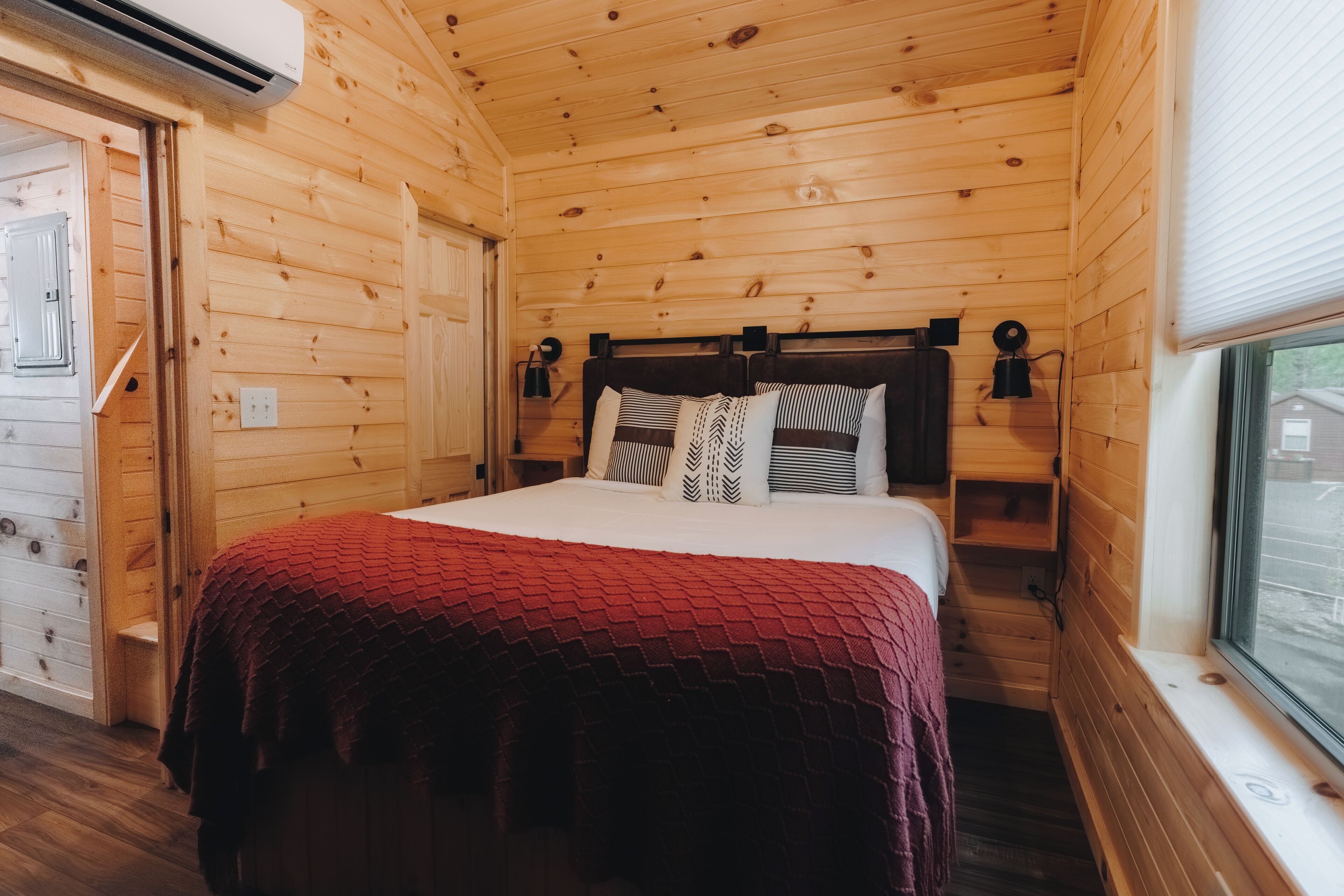 A wooden cabin bedroom with a bed, a window, and a door.