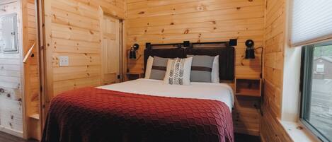 A wooden cabin bedroom with a bed, a window, and a door.