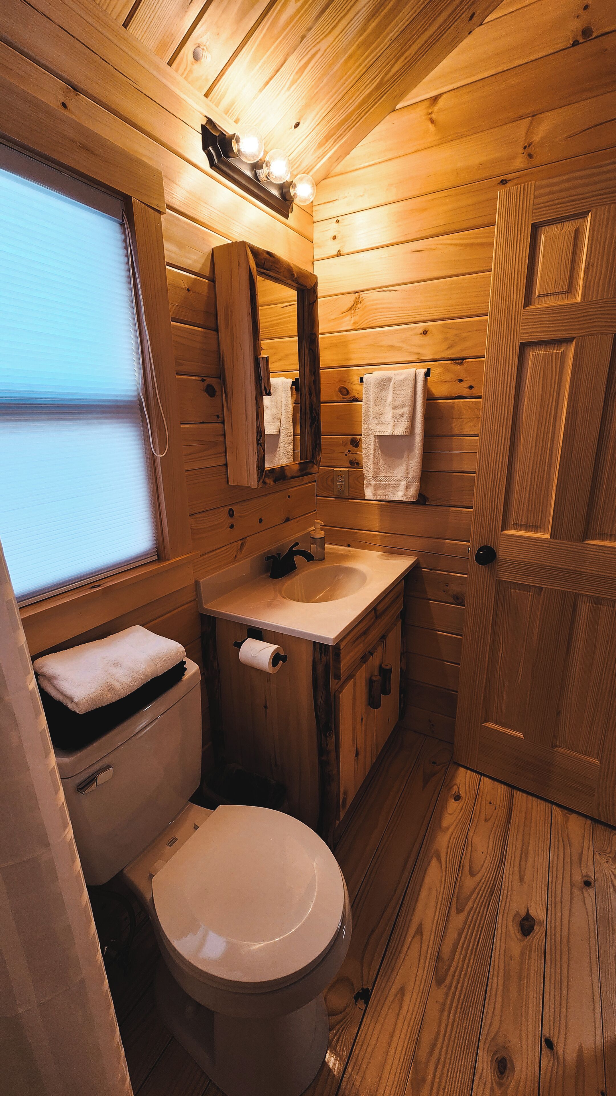 Une petite salle de bain en bois comprenant des toilettes, un lavabo et un miroir.