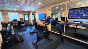 Un gimnasio con equipo de ejercicio, un televisor y un espejo grande.