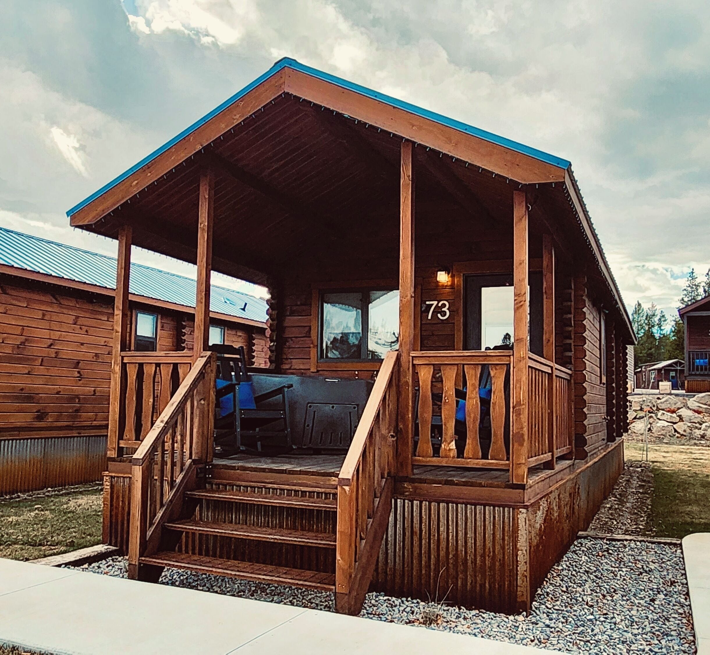 A wooden cabin with a porch, number 73, and a view of the surrounding area.