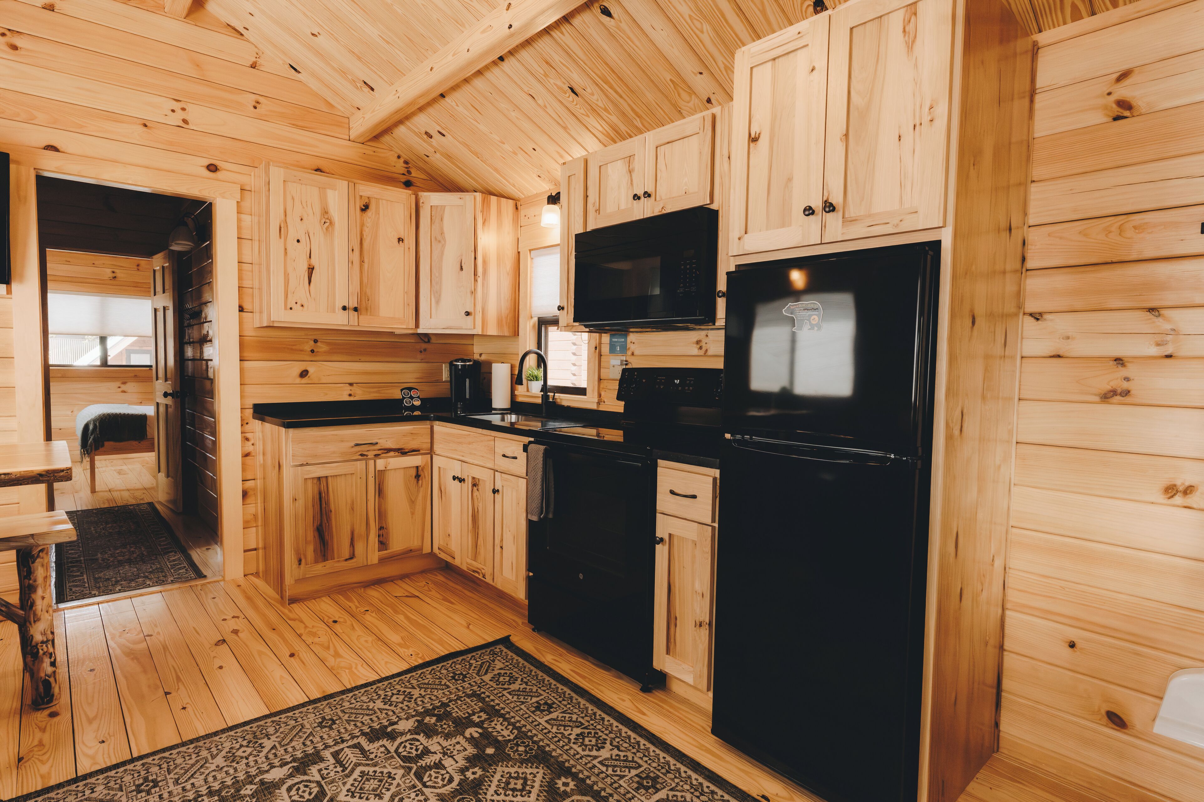 Ein Holzhäuschen im Inneren mit Küchenbereich, der Holzschränke, einen schwarzen Kühlschrank, eine Mikrowelle und eine Kaffeemaschine zeigt.