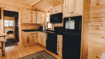 A wooden cabin interior with a kitchen area featuring wooden cabinets, a black refrigerator, a microwave, and a coffee maker.