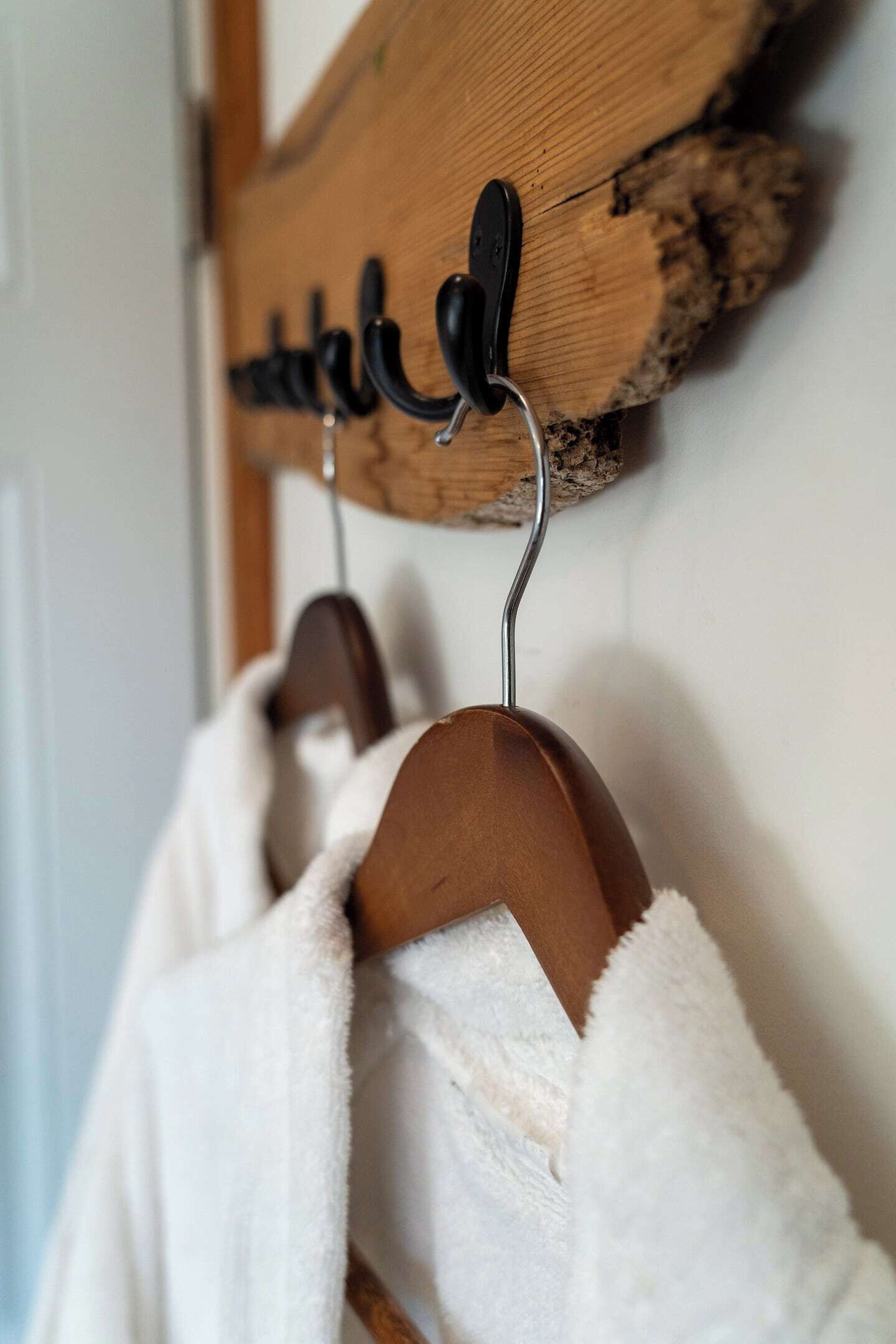 A wooden coat rack with hooks, holding two white robes.