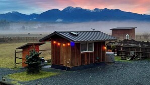 A rustic wooden cabin with a metal roof, surrounded by a wooden fence, and a small shed nearby. - Blue Moon Tiny House | Hot Tub · Sauna · Olympic Views (Port Angeles)
