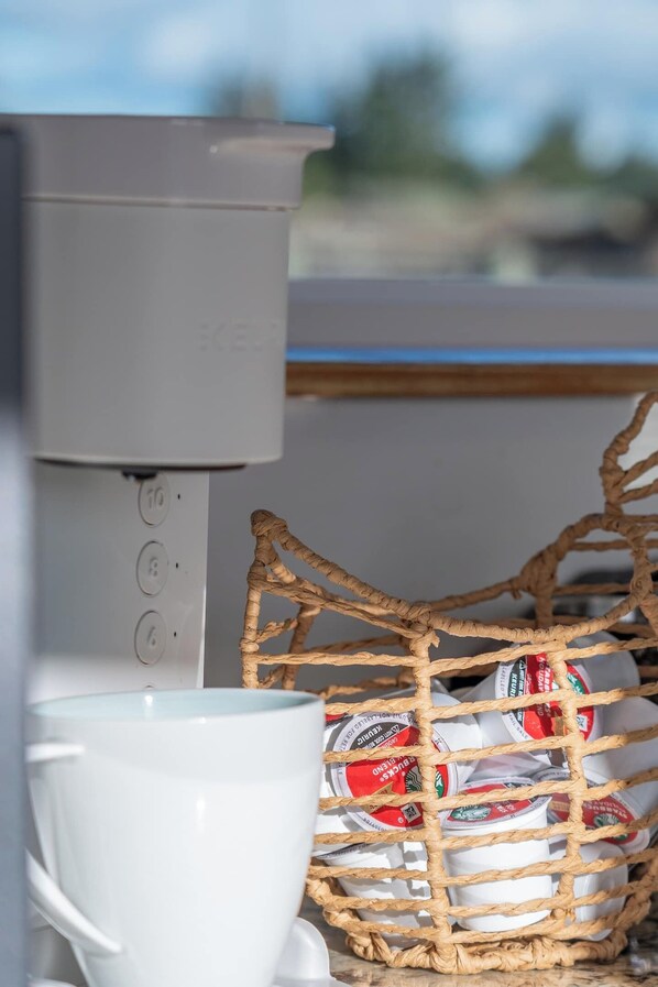 A coffee machine, a white cup, and a basket of coffee pods.