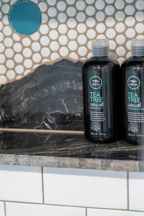Two bottles of Tea Tree Special Shampoo and Conditioner on a tiled countertop.
