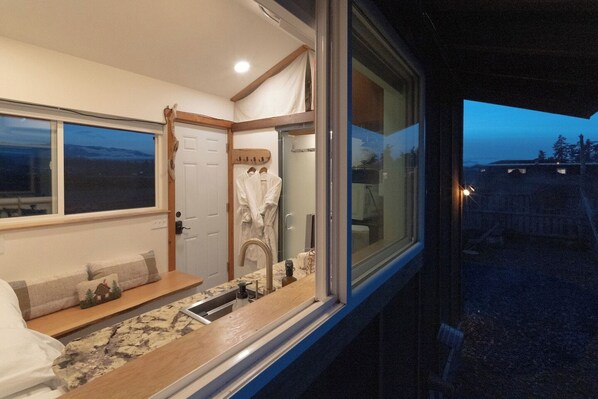 A compact bedroom with a large window, a built-in sink, and a bench with pillows.