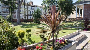 Un jardín bien cuidado con diversas plantas, una palmera y un edificio de ladrillo con porche.