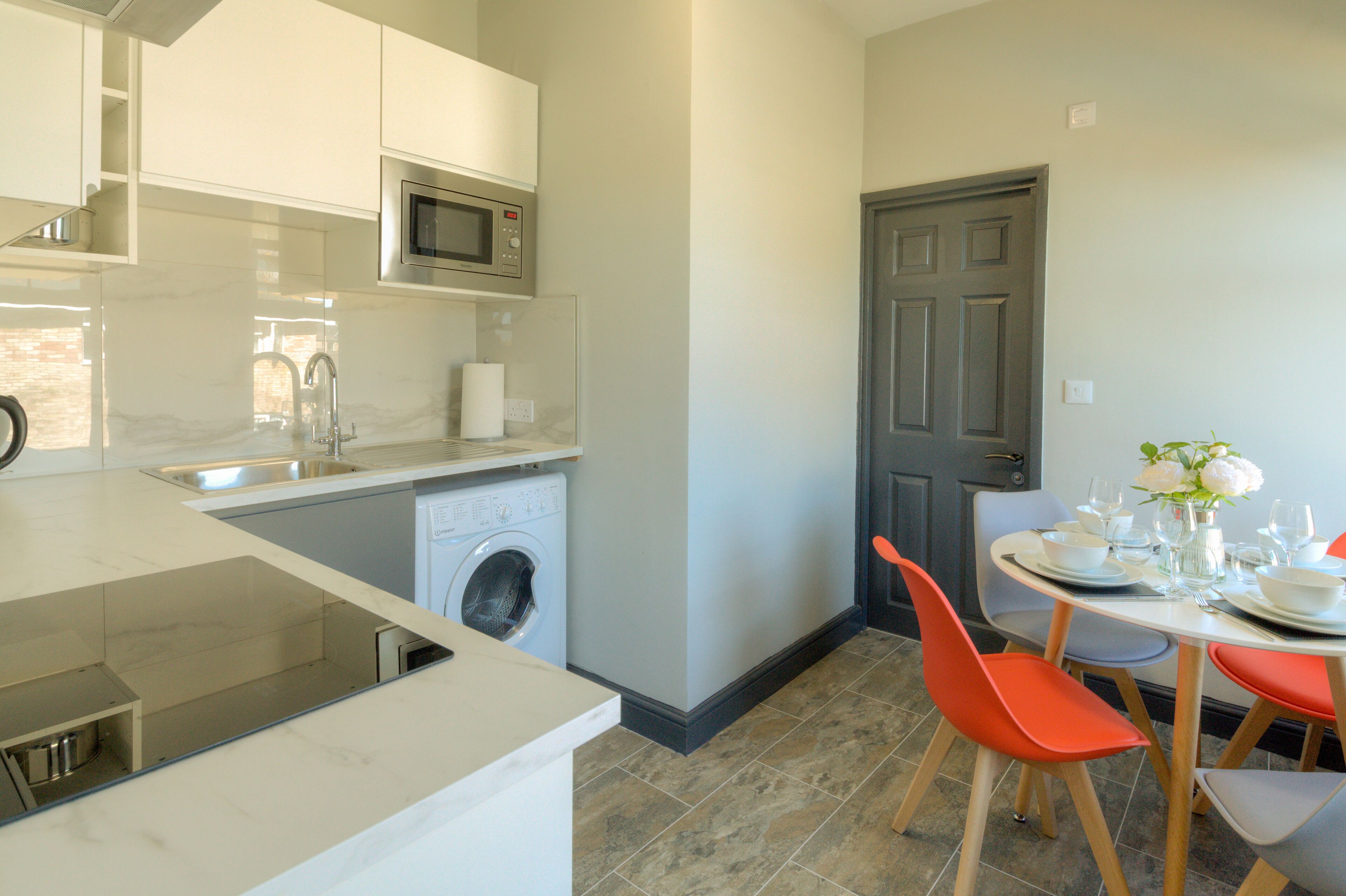 A modern kitchen with a built-in washing machine, a microwave, and a dining area with a table set for four.