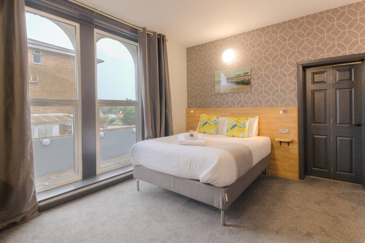 Une chambre d’hôtel avec un grand lit, une vue par la fenêtre, une tête de lit en bois et une porte.