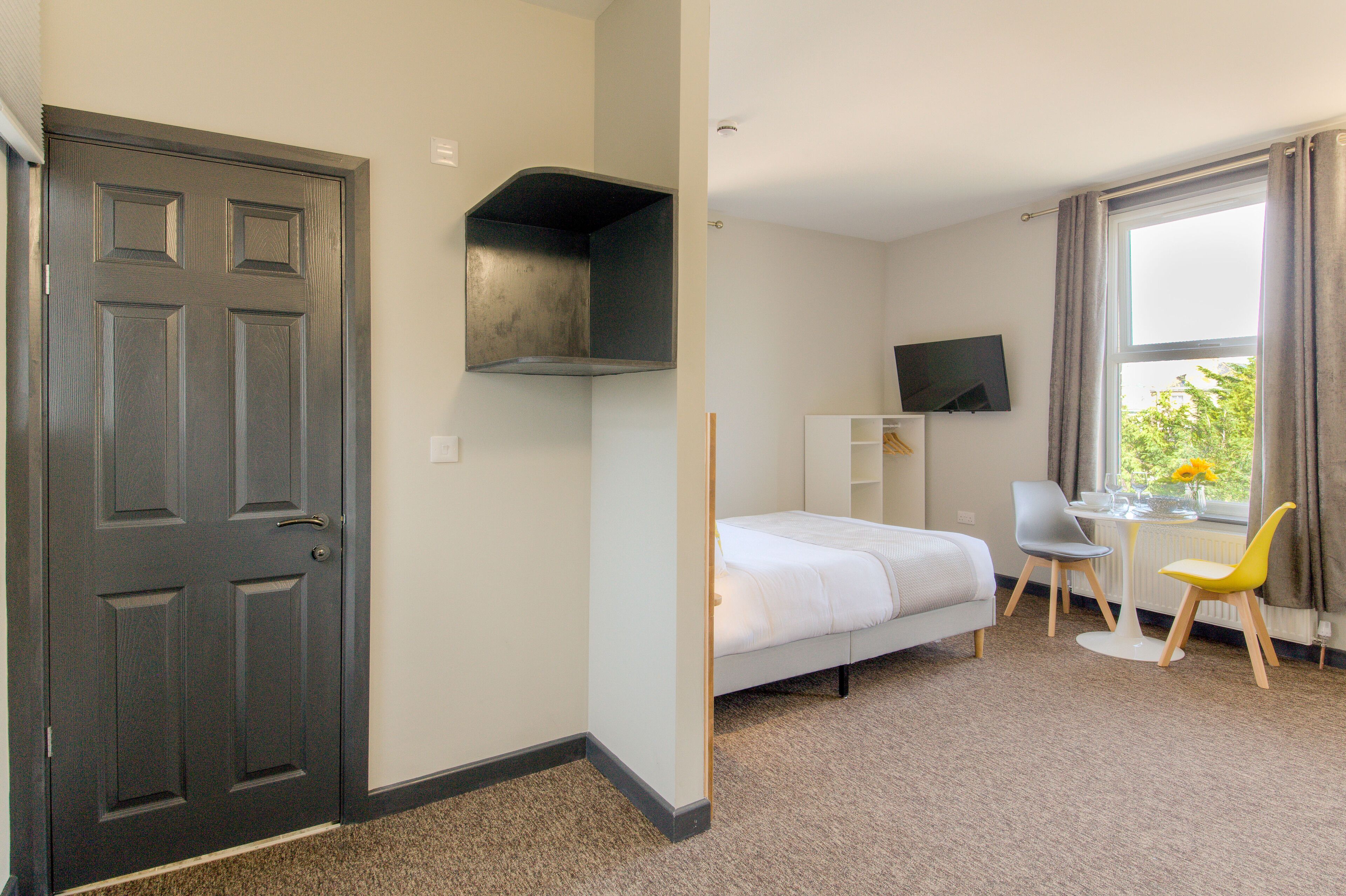 Ein Hotelzimmer mit Bett, Schreibtisch, Stuhl, Fernseher und einem Fenster mit Vorhängen.