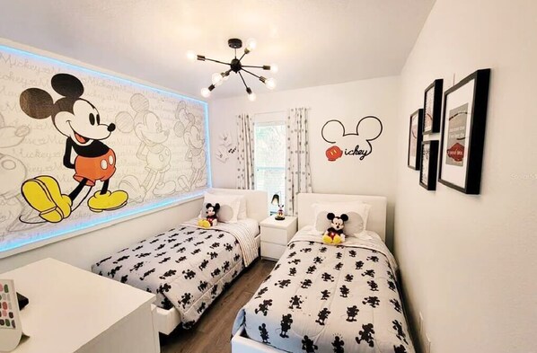 A children's room with two beds, Mickey Mouse wall art, and a ceiling light fixture. - Getaway for SALE 3BR Villa w/Pool&BBQ Themed Rooms near Disney (Kissimmee)