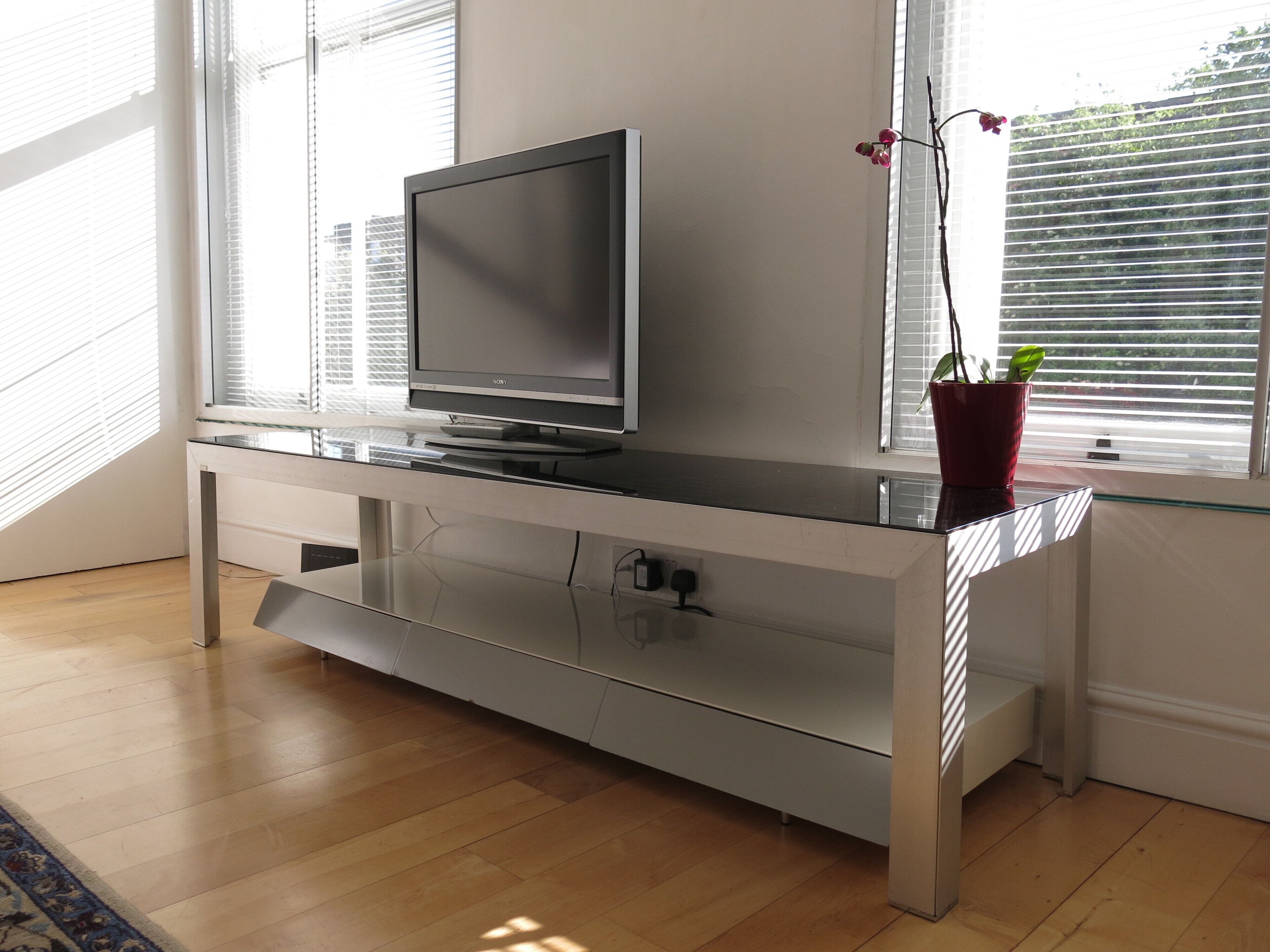 A modern entertainment unit with a flat-screen TV, a glass shelf, and a potted plant.
