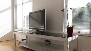 A modern entertainment unit with a flat-screen TV, a glass shelf, and a potted plant. - Chic Flat in Kentish Town, 5min to Hampstead Heath (London)