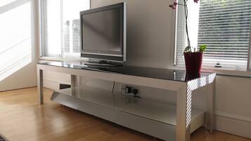 A modern entertainment unit with a flat-screen TV, a glass shelf, and a potted plant.