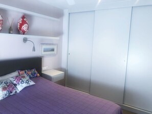 Une chambre à coucher comprenant un lit, une table de chevet, un téléviseur fixé au mur et un placard à portes coulissantes.
