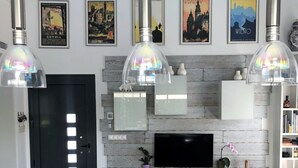 A modern living room with a grey sofa, a flat-screen TV, and a fireplace. There are framed pictures on the wall and a bookshelf to the right. - Stunning villa, large private pool, 8' from beautiful beach (Quesada)