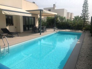 Une piscine dotée d’un espace détente couvert, d’une chaise longue et d’une table.