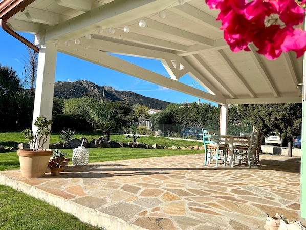 A covered patio with stone flooring, outdoor furniture, and potted plants.