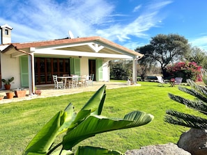 Une maison dotée d’un patio couvert, d’une pelouse et de plantes en pot.
