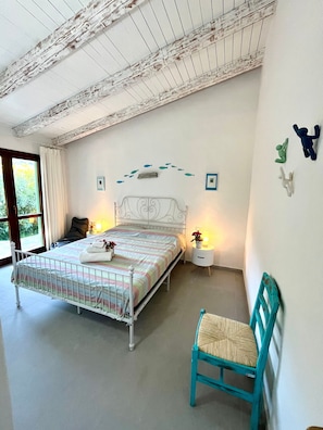 Une chambre à coucher comprenant un lit, des tables de chevet, une chaise, une fenêtre et un plafond avec des poutres apparentes.