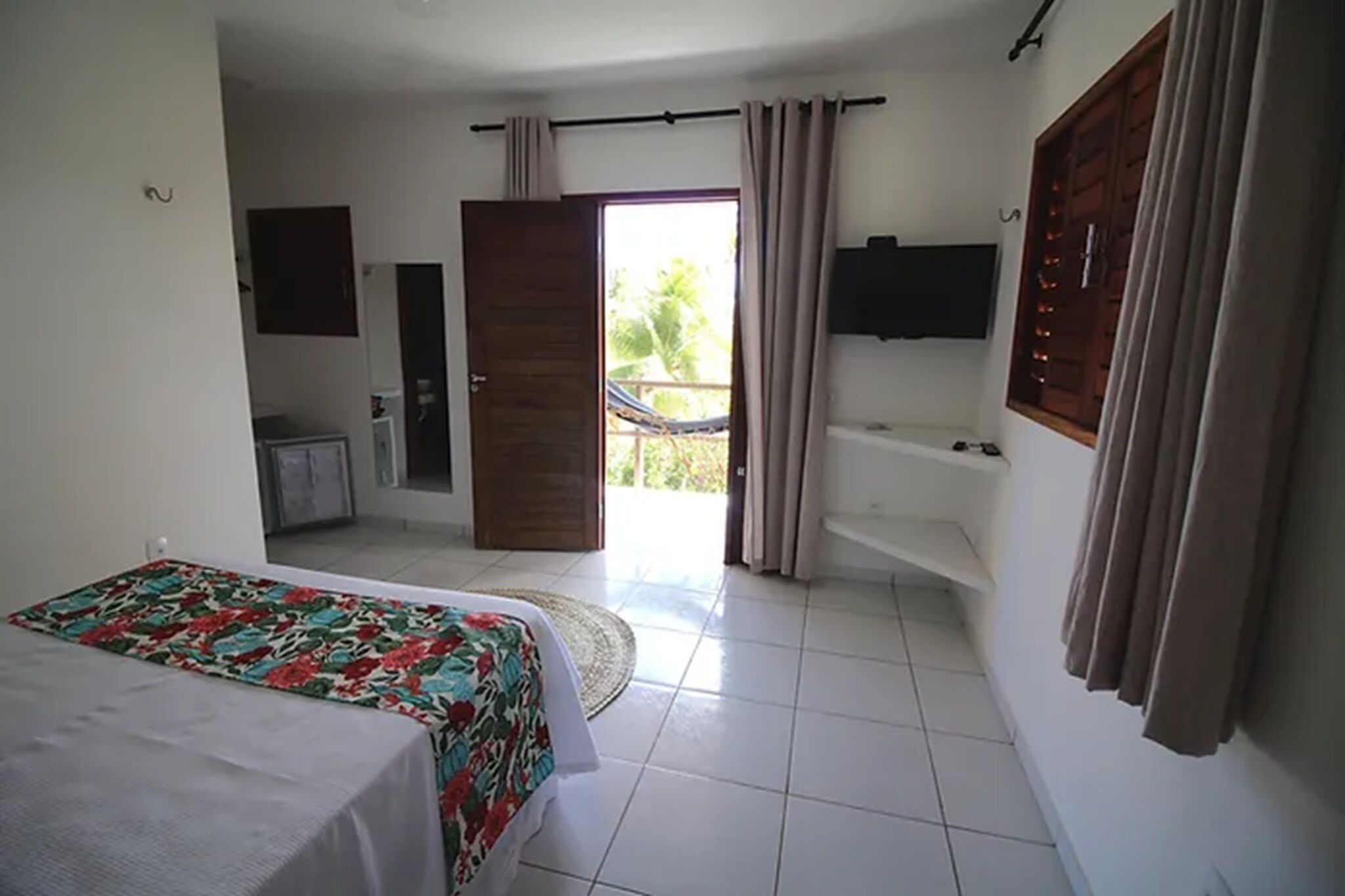 A bedroom with a bed, a bathroom with a bathtub, a TV, and a balcony with curtains.