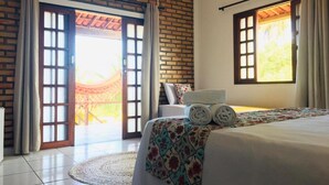 Ein Hotelzimmer mit Backsteinwand, einem Bett mit floralem Überwurf und Blick durch eine Glastür sowie einem Fenster mit Vorhängen.