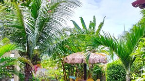 Ein Garten mit einem Pflasterweg, Palmen und einem Gazebo mit Strohdach.