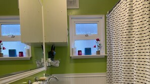 A bathroom with a white sink, toilet, and bathtub. There are two windows with curtains, a mirror, and a towel rack. - Dog 🐾 friendly home with a view 🌅 near airport ✈️ (Des Moines)