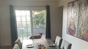 A dining room with a large wooden table, chairs, and a dog sitting by the window. - Dog 🐾 friendly home with a view 🌅 near airport ✈️ (Des Moines)