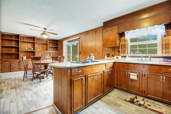 A kitchen with wooden cabinets, a dining area with chairs, a ceiling fan, and a window with a view. - Perfect Southern Pines Getaway Near Pinehurst! (Aberdeen)