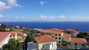 A coastal town with terracotta-roofed buildings, a clear view of the sea, and a hilly landscape in the background. - Holiday Apartment in Madeira (Caniço)