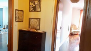 A room with a wooden dresser, a cityscape painting, and a tree painting on the wall. - Holiday Apartment in Madeira (Caniço)