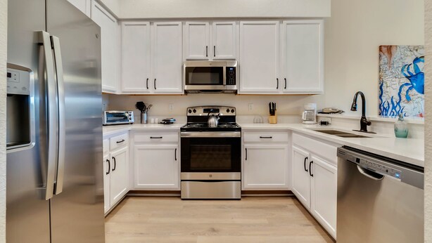 A modern kitchen with white cabinets, stainless steel appliances, and a wooden floor. - Caribe Cove -Gorgeous and Cozy   Close to Disney (Kissimmee)
