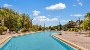 A clear blue swimming pool with lounge chairs and umbrellas, surrounded by trees and a clear sky. - Caribe Cove -Gorgeous and Cozy   Close to Disney (Kissimmee)