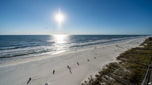 A beach with a clear sky, the sun shining, and a few people walking.