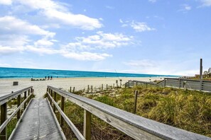 Une promenade en bois qui mène à une plage, avec un ciel dégagé.