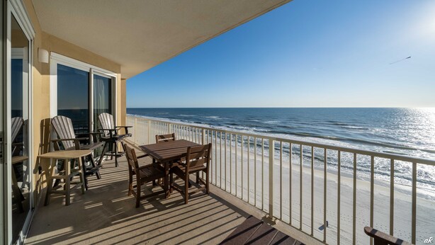 A balcony with a view of the ocean, furnished with wooden chairs and tables.