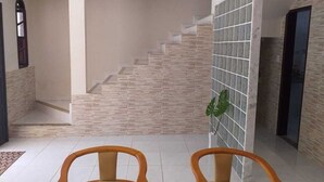 Eine Treppe mit Steinstufen führt zu einer Zwischenebene, an einer Wand ist ein Gittermuster zu sehen, und im Vordergrund stehen zwei Holzstühle.