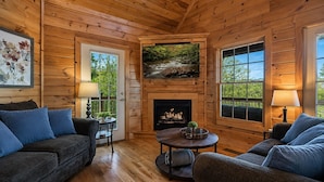 A log cabin interior with a fireplace, wooden walls, and large windows. - Ranked Top 1% Cabin-Location-Views-Hot Tub-Games (Pigeon Forge)