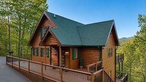 A log cabin with a balcony, a porch, and a view of the surrounding forest. - Ranked Top 1% Cabin-Location-Views-Hot Tub-Games (Pigeon Forge)