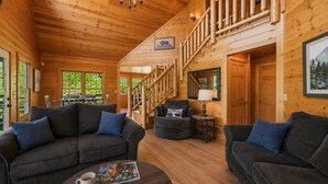 A log cabin interior with a sofa, armchair, coffee table, and a staircase. - Ranked Top 1% Cabin-Location-Views-Hot Tub-Games (Pigeon Forge)