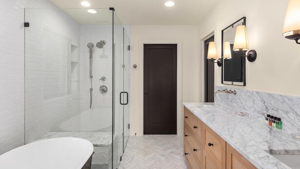 A modern bathroom with a glass-enclosed shower, a white bathtub, and a marble countertop vanity.